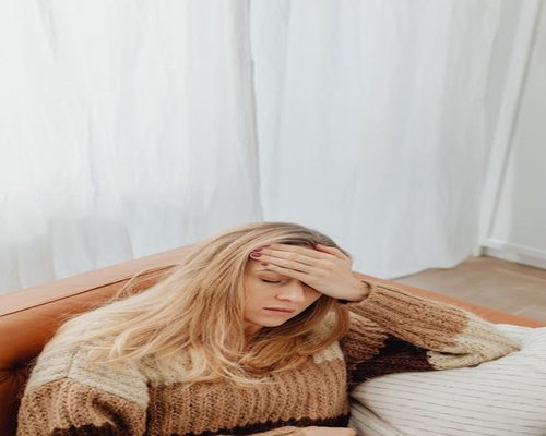 A person rubbing their forehead gently while sitting on a sofa