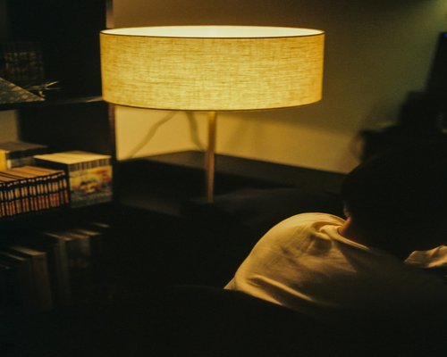 A person reading a book on a comfortable chair with soft light coming from a nearby lamp