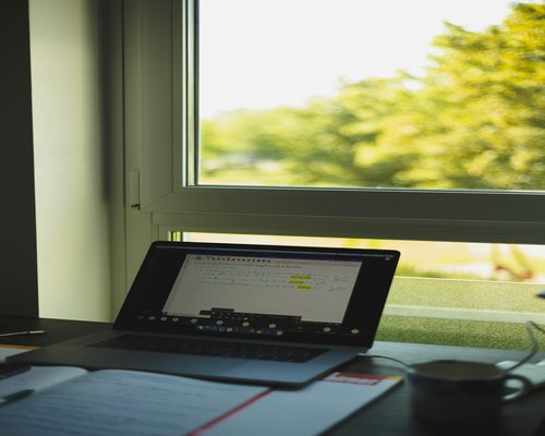 A laptop on a desk showing an empty spreadsheet next to natural window light